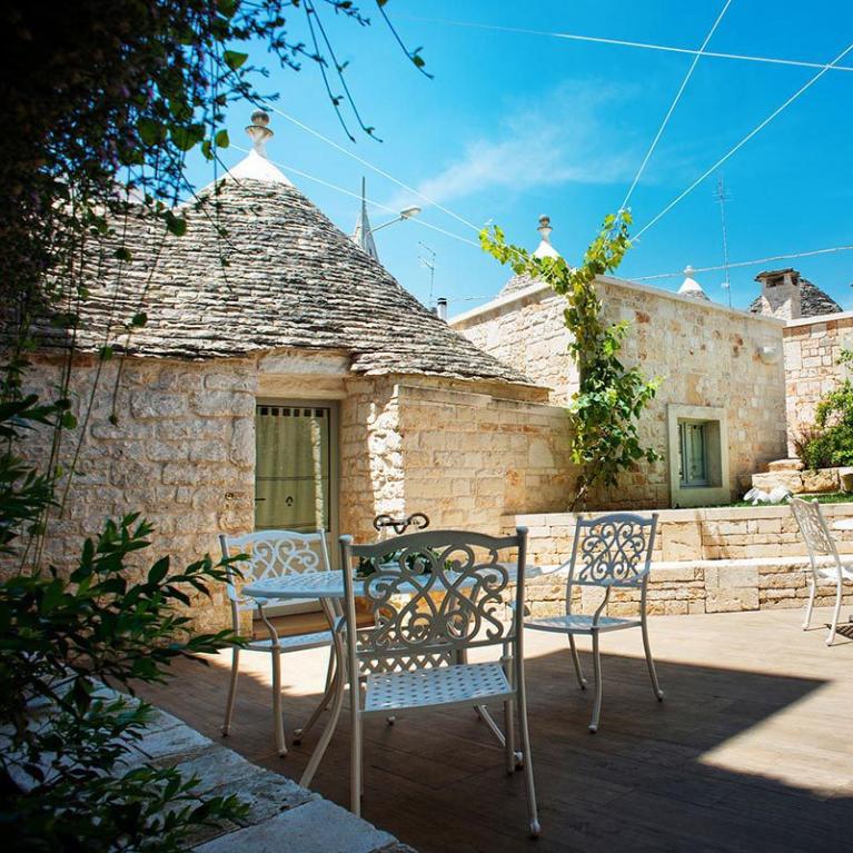 Cour avec trulli, chaises et tables en fer forgé, ciel dégagé.