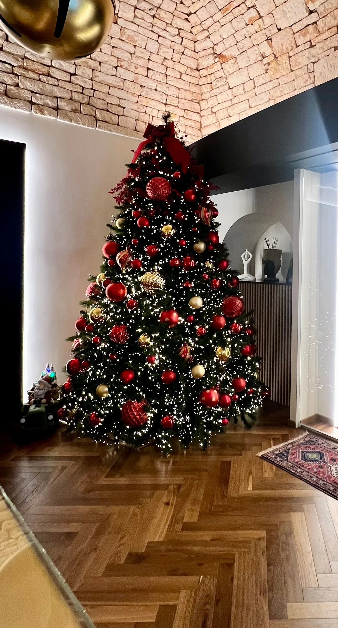 Christmas tree with red and gold baubles and white lights in the reception hall of Palazzo Scotto, under a stone vaulted ceiling with a large gold bell hanging from it, on a herringbone wood floor.
